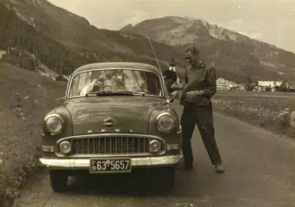 Nuori mies ja auto, taustalla Alppeja.