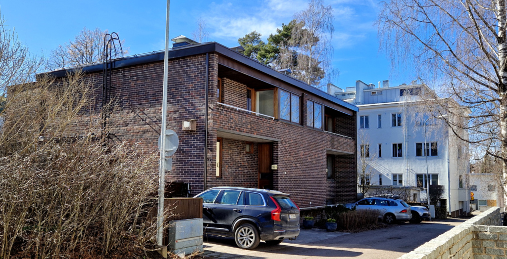 Pientalo pihakadun varrella, edessä autoja parkissa.