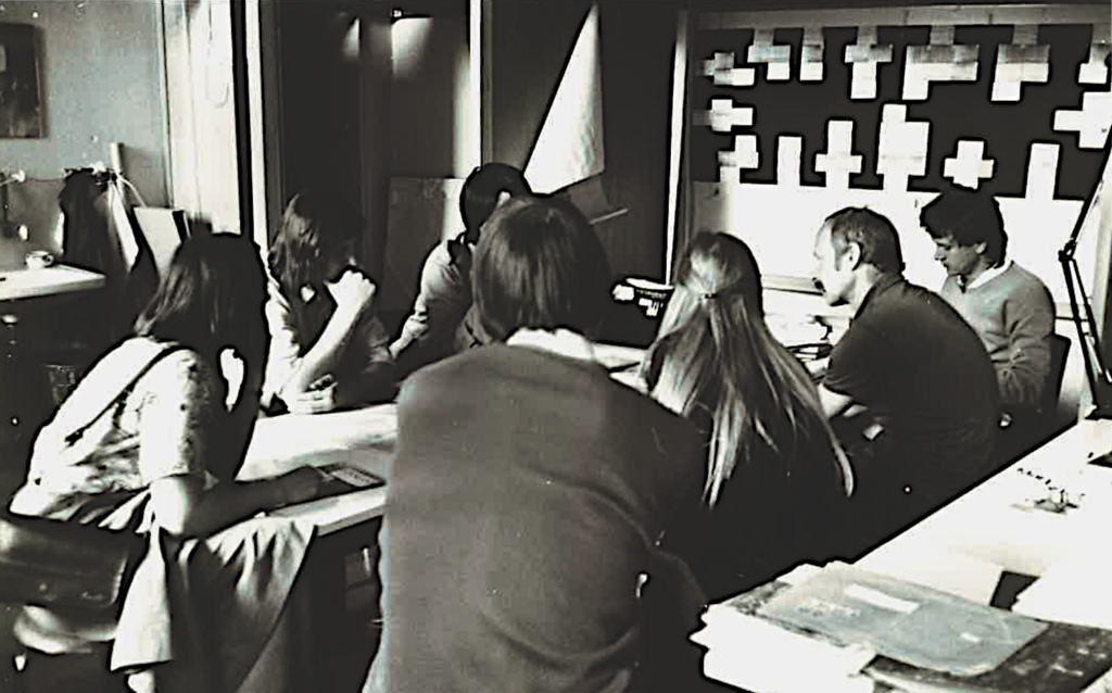 Arkkitehtiopiskelijat ohjaajineen pöydän ääressä.