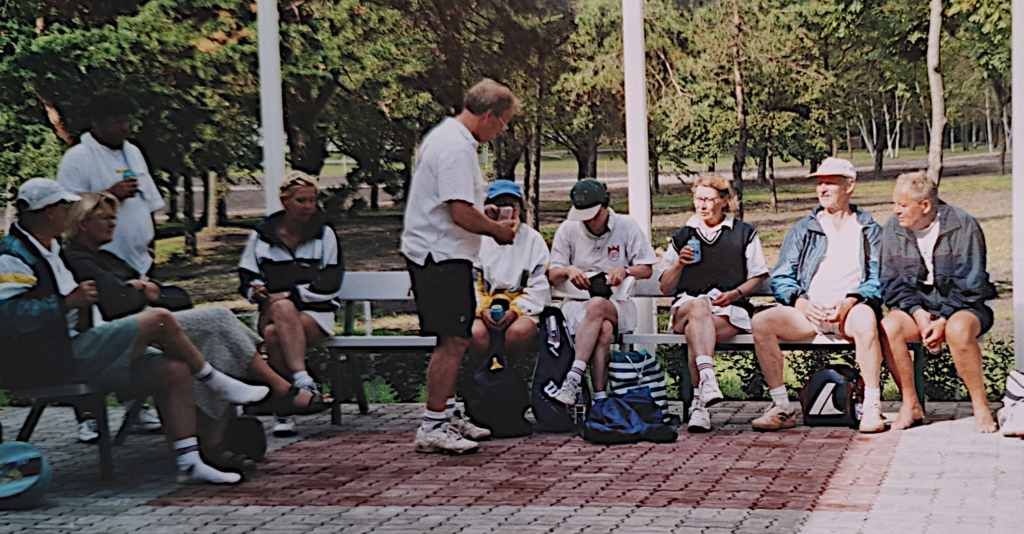 Joukko tenniksen harrastajia tauolla puiston penkeillä.