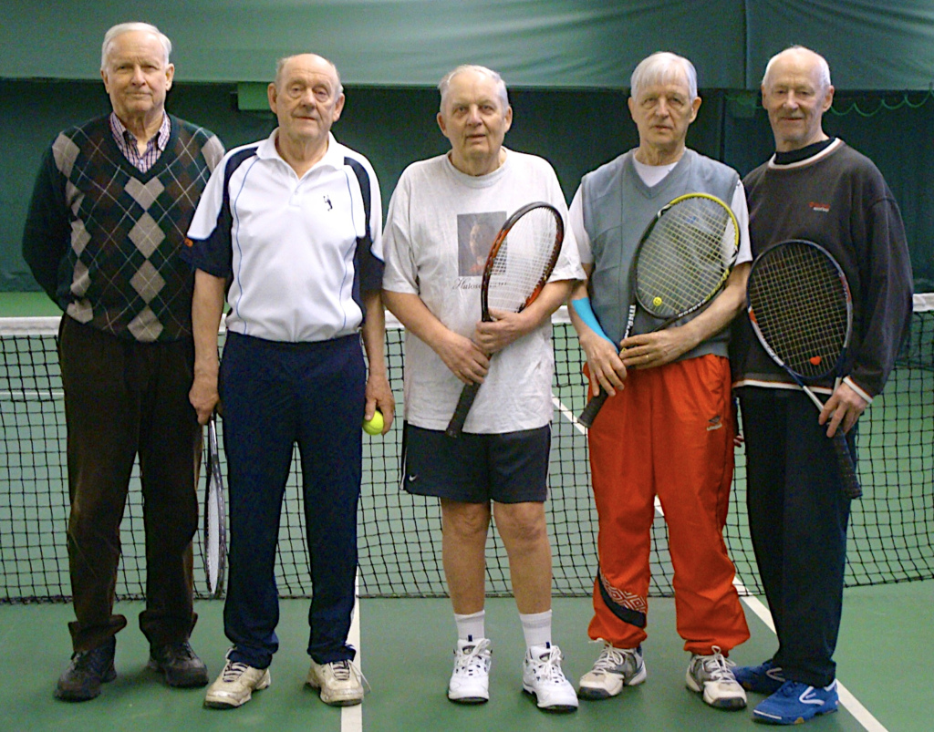 Viisi miestä poseeraa tennishallissa.